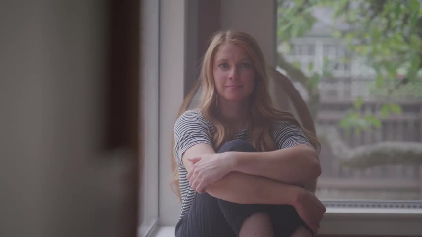 Woman sitting with her arms wrapped around her knees briefly looks out the window