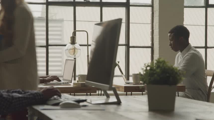 A woman walks past people typing at their desks