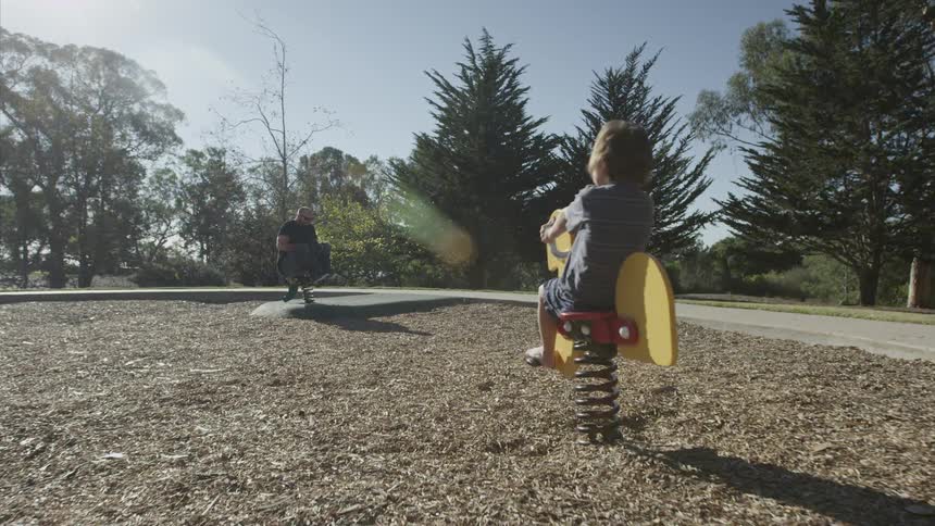 A man and child rock on playground toys