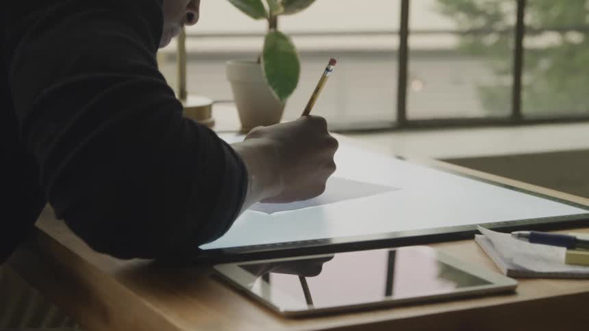 Man uses a pencil to draw on a lighted desk
