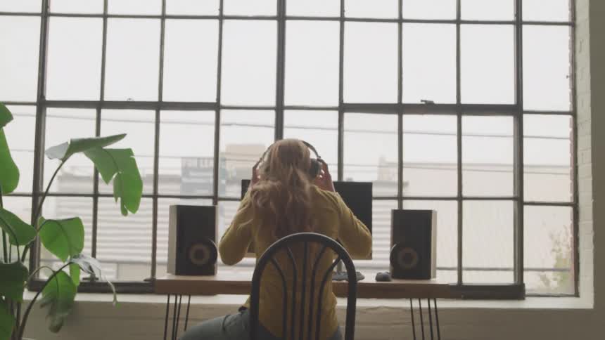 Woman puts on headphones as she sits in a chair then dances in her seat