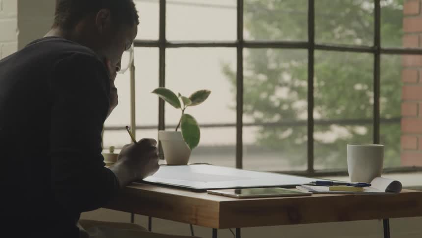 A man is sitting at a desk drawing on paper