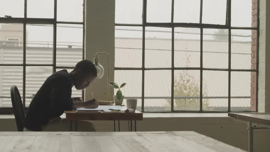 Teenager sits at a table near the window and writes