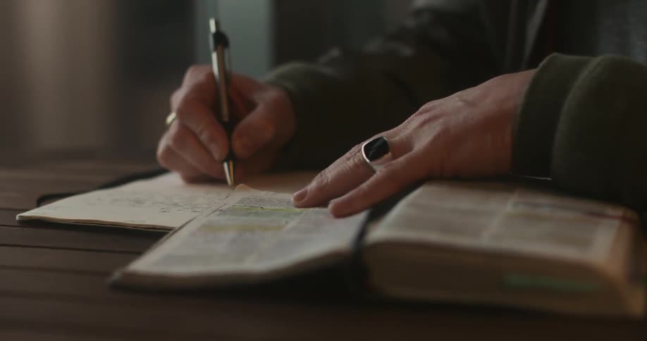 A person sits at a desk with a bible and a notepad that they are writing on