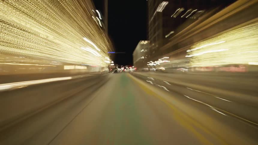 A blurred nighttime drive through a city street reveals streaks of light and passing buildings