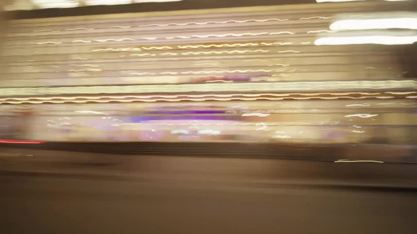 A spedup nighttime cityscape blurs past in streaks of colorful light as seen from a moving vehicle