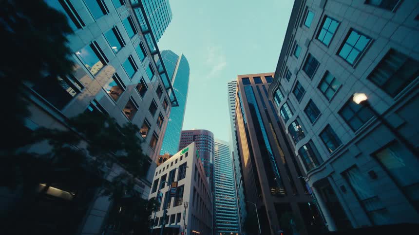 A cluster of tall city buildings with diverse architectural styles and colors from blue glass facades to traditional stone and brick structures emphasizing their towering height against a clear sky and creating a sense of urban grandeur