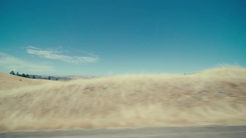 A landscape shot shows rolling hills under a clear blue sky with a dust cloud obscuring the foreground and a glimpse of trees in the distance