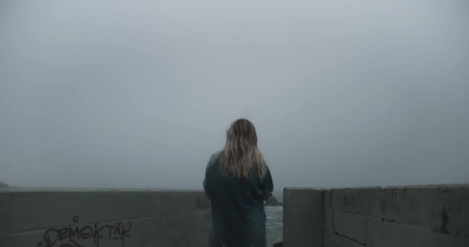 A woman is standing by the water near a brick pier