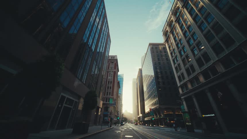 A city street stretching into the distance between tall buildings with sunlight illuminating the far end