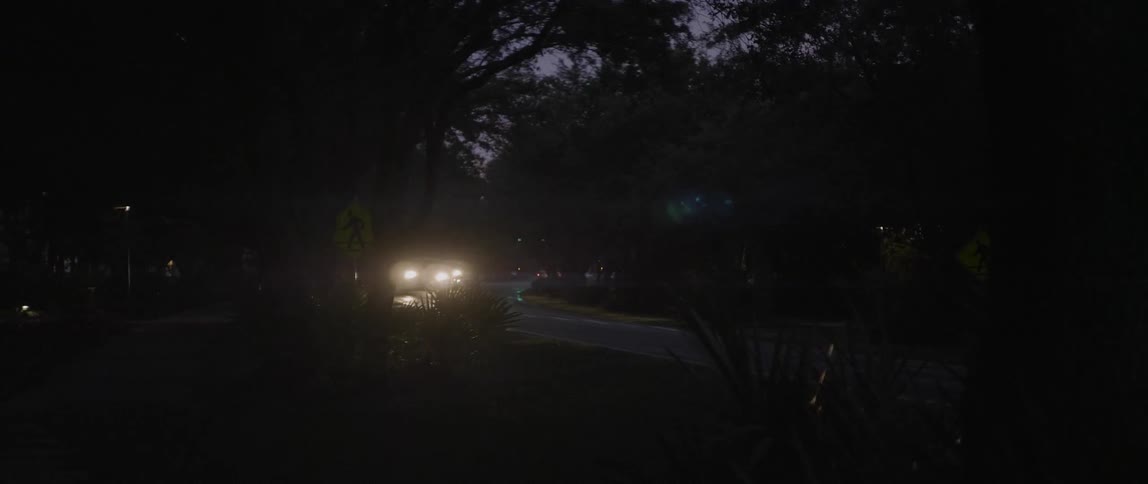 Vehicles driving down a rural road with their headlights on because it's dark