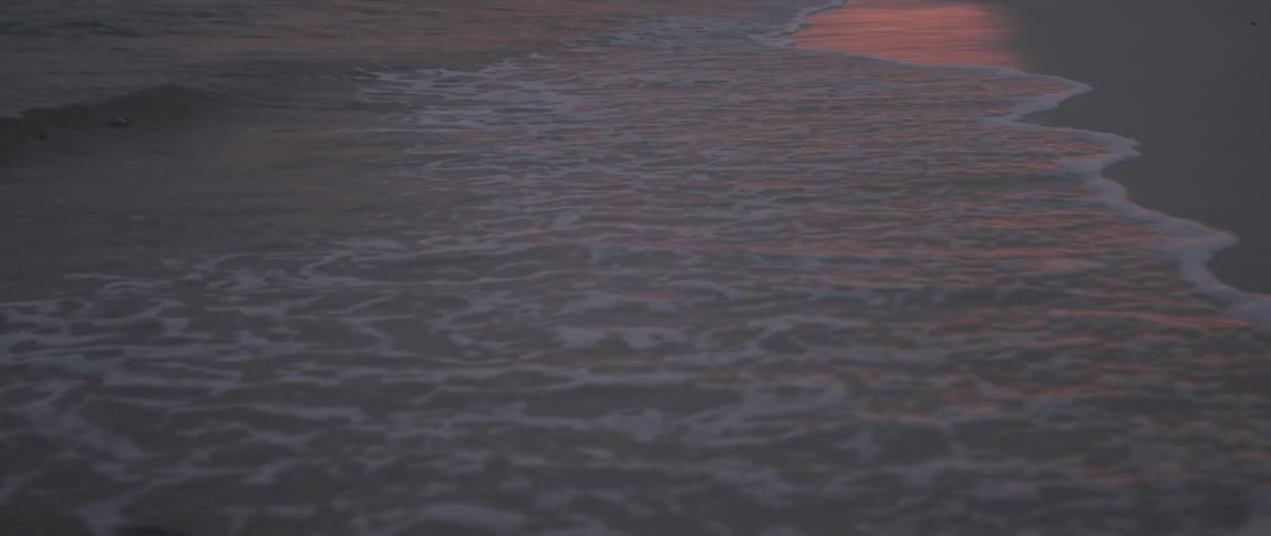 Waves break and foam on the beach sand at sunset