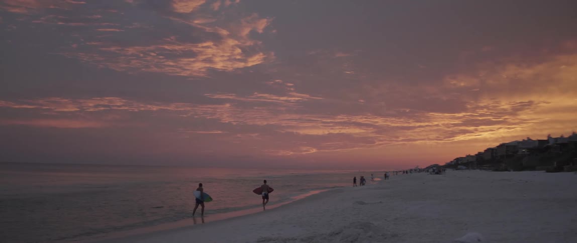 Surfers and other beachgoers walk on a beach at sunset