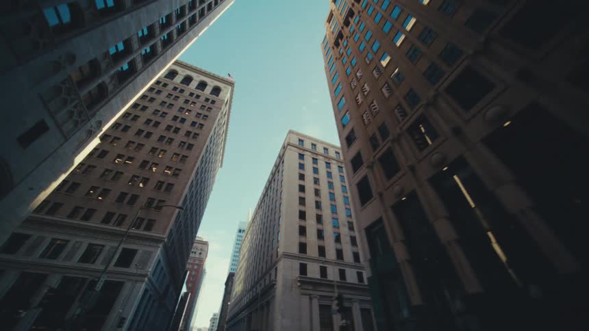 Towering city buildings with varied architectural styles from classic stone facades to modern glass windows against a clear blue sky