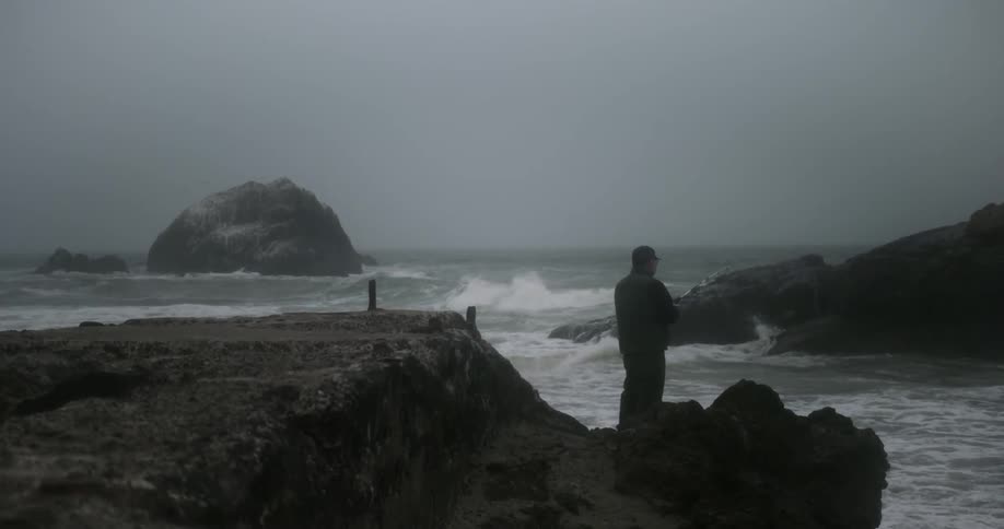 A man is fishing off the rocks by the rough coast