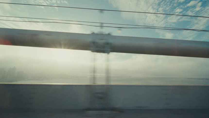 A guard rail is being passed while moving down a street with the blue sky behind it