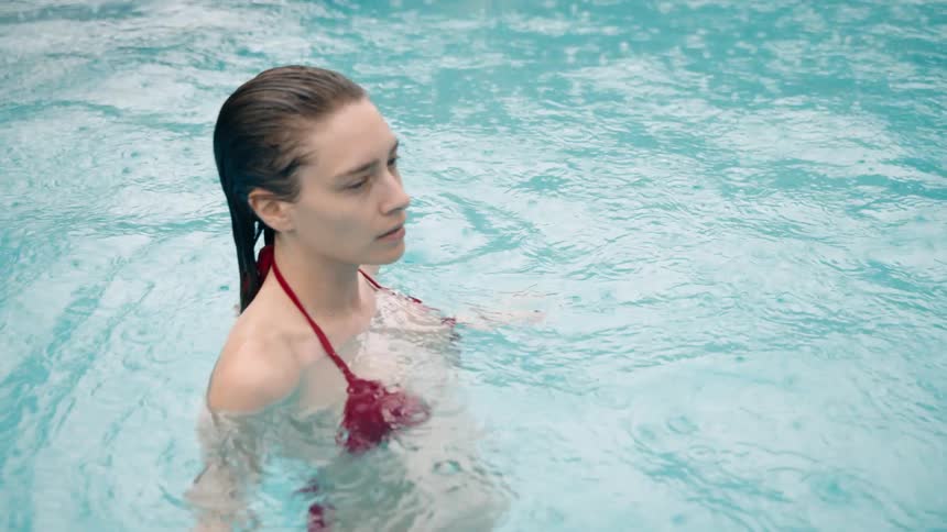 Woman in a red bikini swimming in a pool with rain falling around her creating tiny bubbles