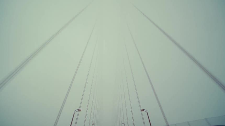 Driving beneath the golden gate bridge as its iconic red towers disappear into the thick mist and fog above