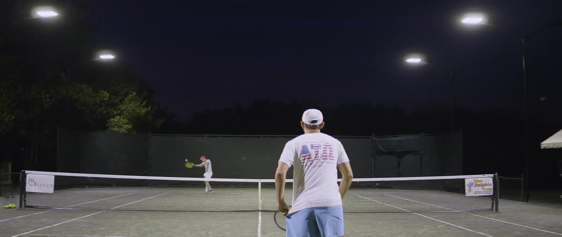 Two people play tennis at night