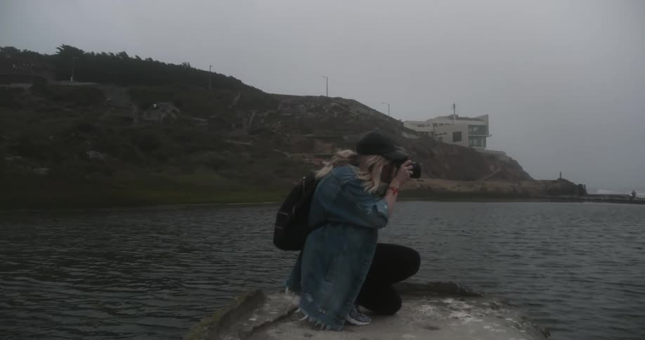 Woman sits on a rock by the water taking photos