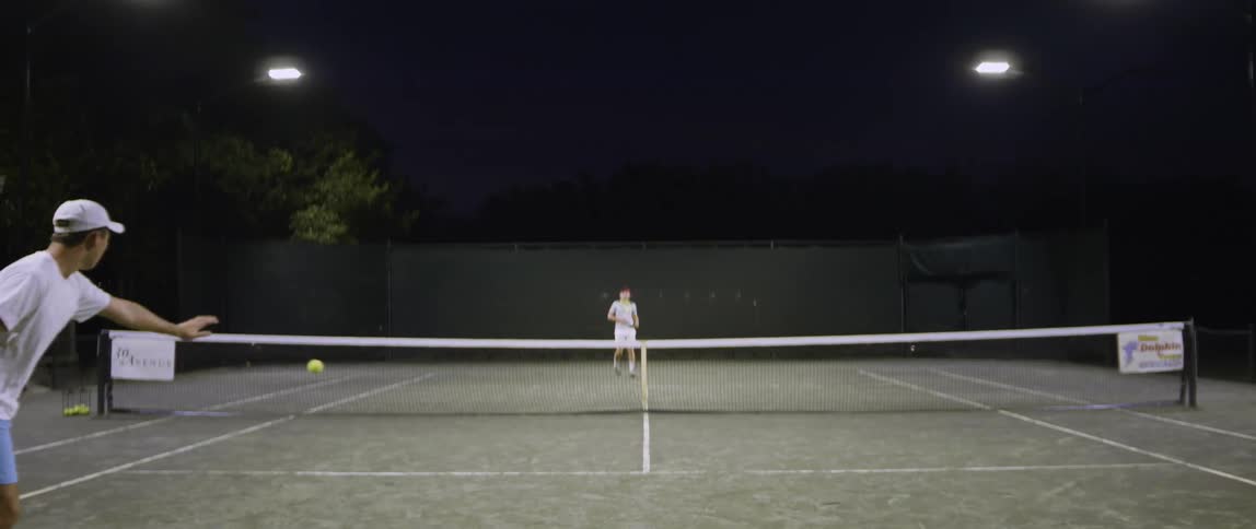 Two tennis players drive the ball back and forth at night