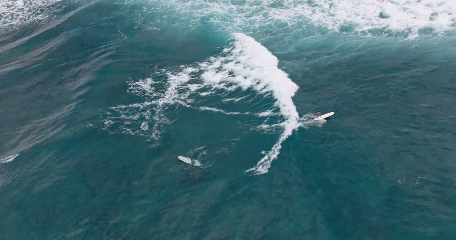 A surfer glides on their board navigating through choppy ocean waves and frothy white foam