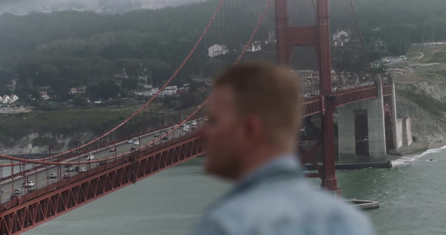 A man stares out by a large bridge