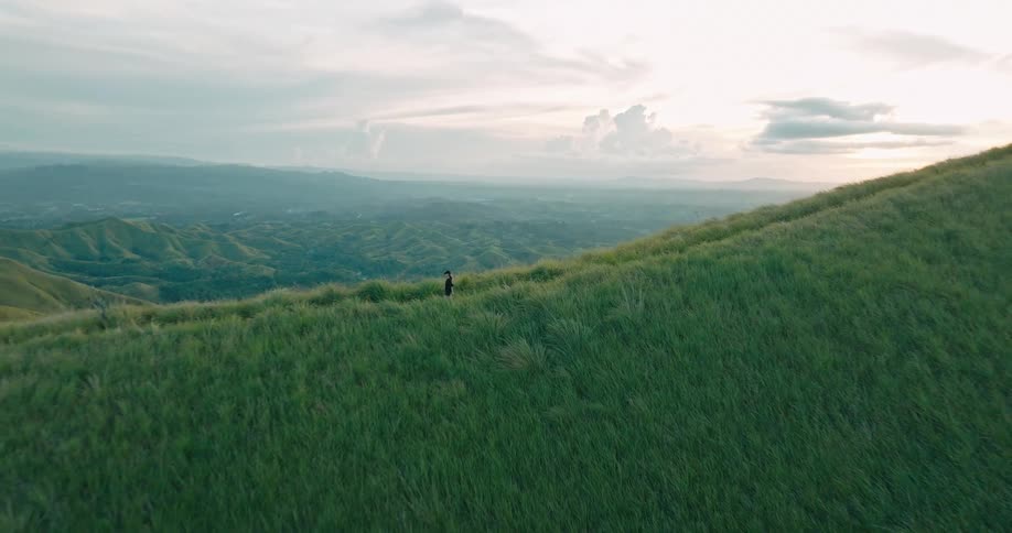 A woman is hiking alone down a grassy hill