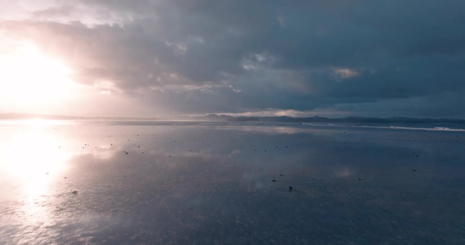 A serene beach landscape at sunset with the sun reflecting off the wet sand creating a mirrorlike effect under a dramatic sky filled with dark moody clouds