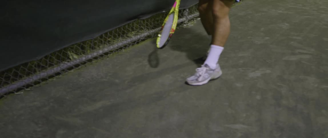 A man is playing tennis bouncing the ball with his racket