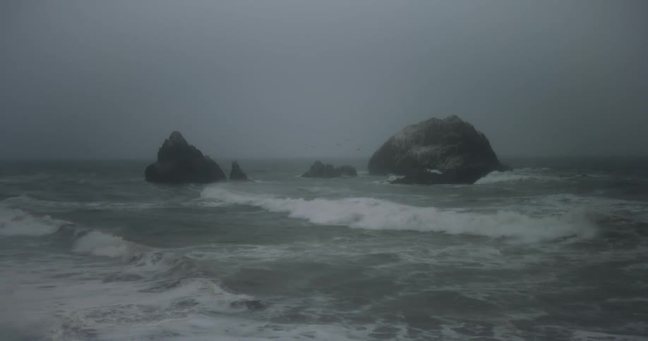 Large waves crash against large rocks in the ocean