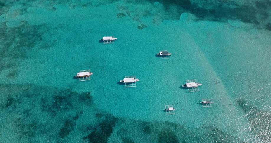 An aerial view of a vibrant turquoise sea dotted with traditional outrigger boats