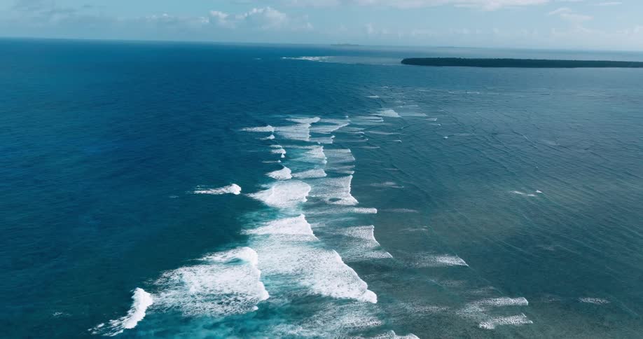 Waves travel across the ocean under a pale blue sky