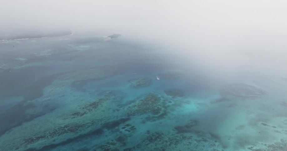 Dense fog partially covers small green tinted islands and the surrounding blue water during the day