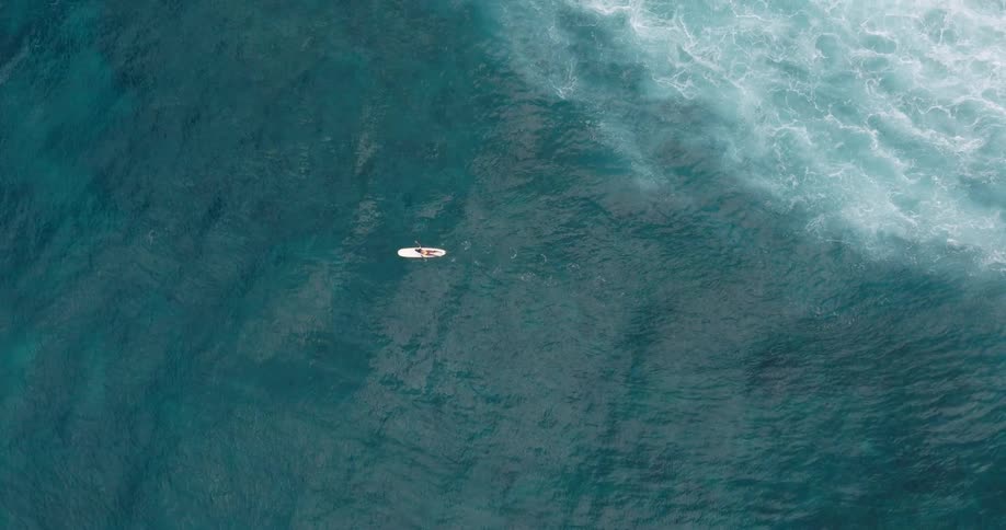 Birds eye view of surfer paddling on a long board in the ocean