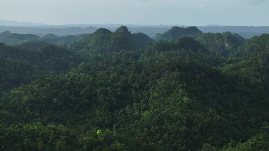 Aerial view glides over lush mountain ranges blanketed in dense green vegetation under a cloudy sky