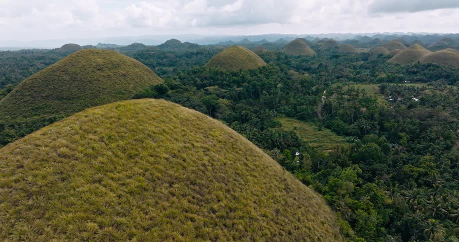 An aerial view over the iconic chocolate hills in the philippines shows hundreds of symmetrical grasscovered mounds rising from dense jungle under an overcast sky
