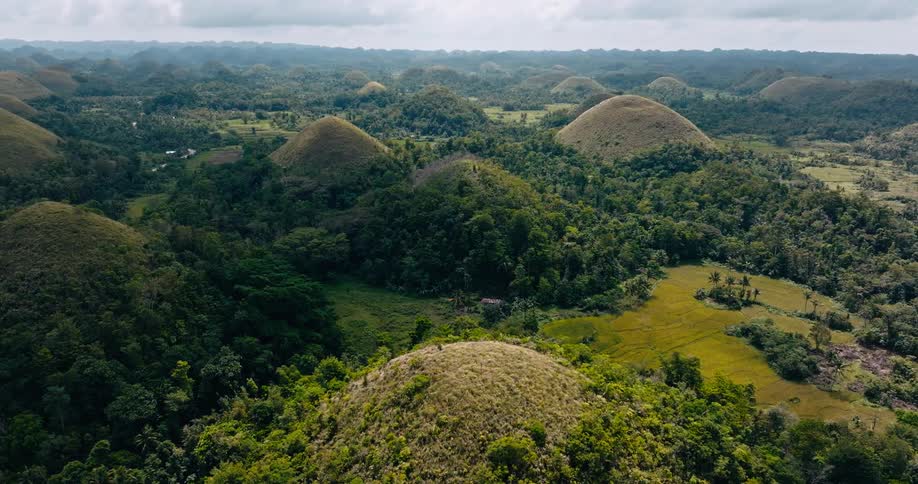 An aerial view reveals the iconic chocolate hills rising from a dense tropical landscape with rounded peaks stretching across the horizon