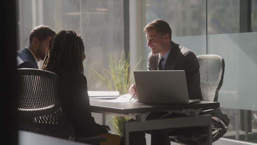 Male office worker discusses a document with his clients while they sit in his office