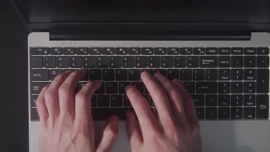 View looking down at a mans hands typing on the keyboard of a laptop computer