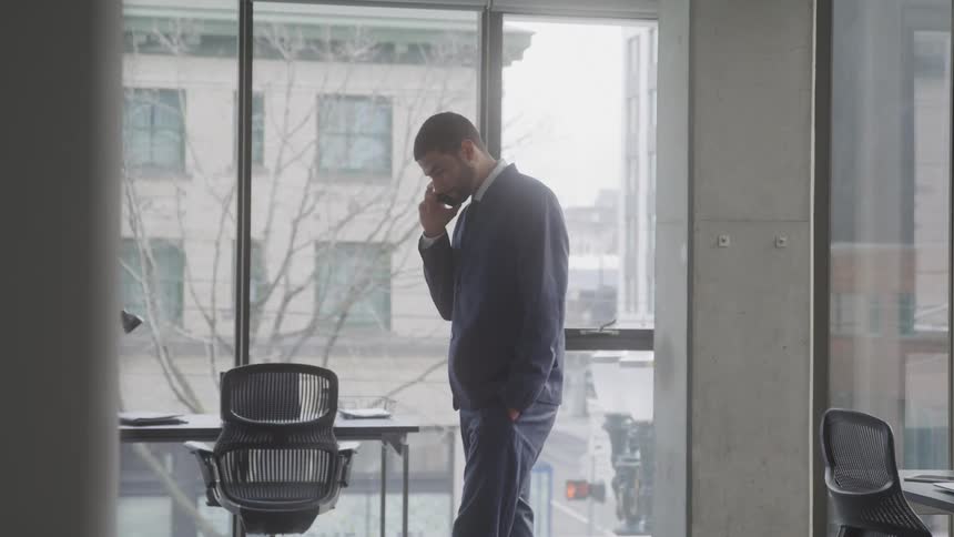 A middle eastern man walks around in a corner office while talking on his smartphone