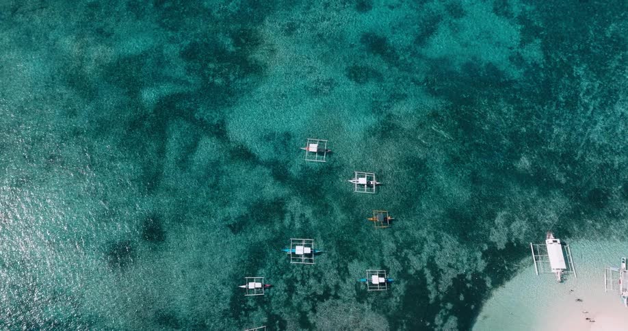 Double outrigger canoes float on translucent blue water on a sunny day