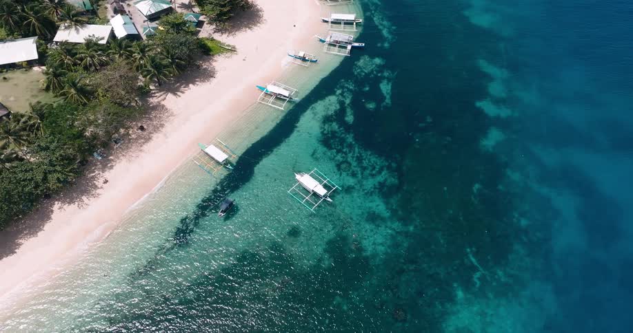 An aerial view of a tropical beachfront lined with palm trees and boats anchored in shallow coralrich waters near white sandy shores