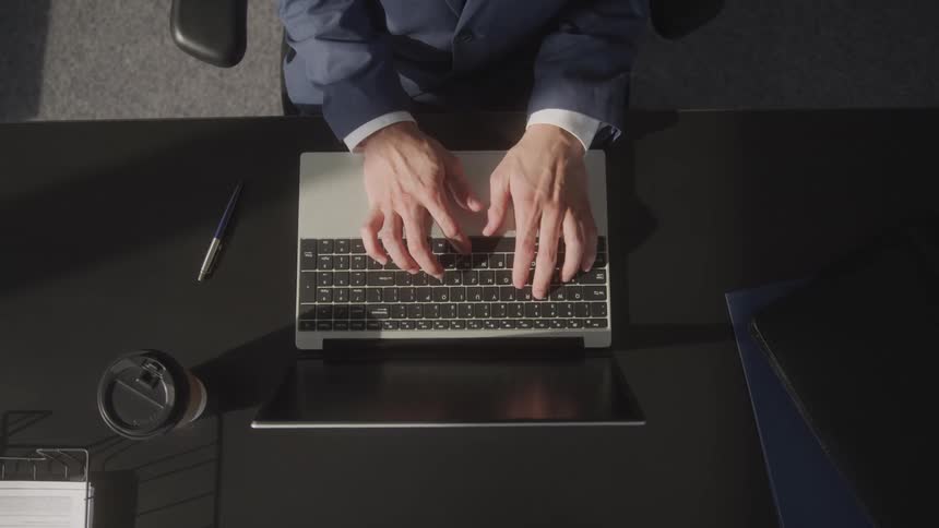 A person is typing on their laptop while sitting at their desk