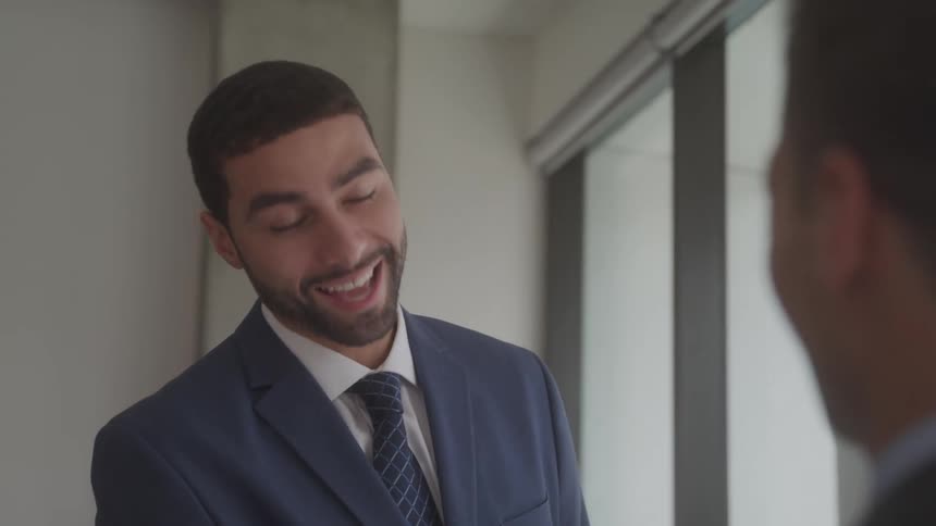 Two businessmen shake hands then smile during a conversation at the office