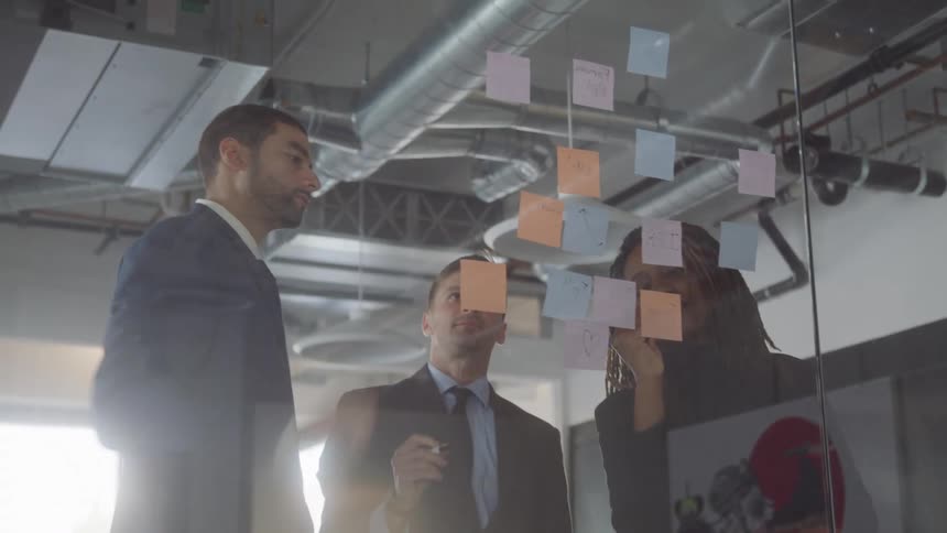 Office workers talk and look at post its on the glass