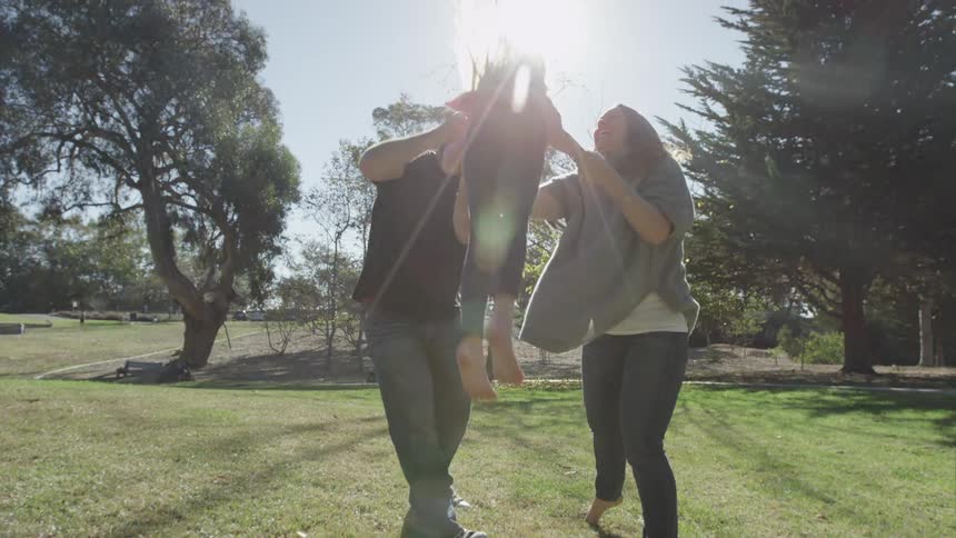 A man and woman swing a child by her arms on a sunny day