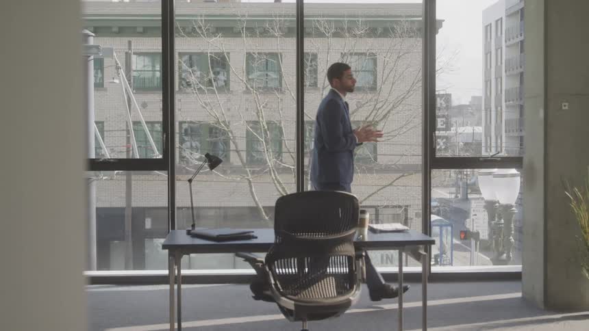Man in a suit walks across an office with floor to ceiling windows