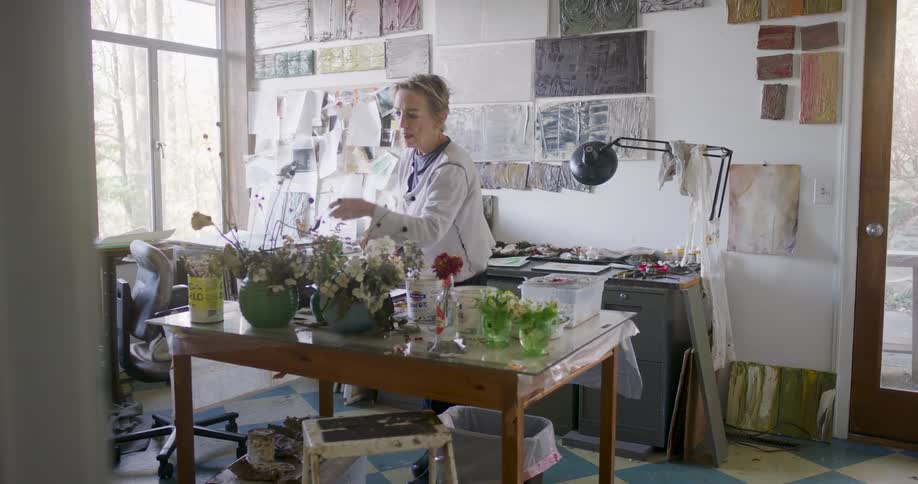 Woman in her workshop looks over the flowers on her work table before selecting a paint
