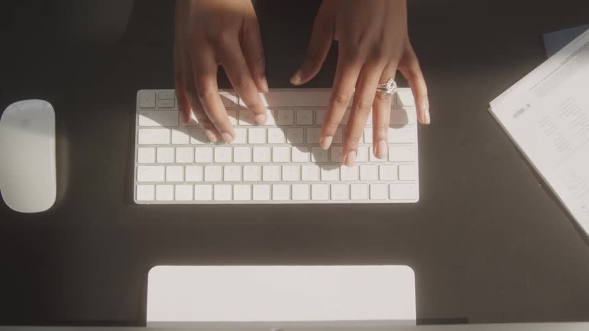 A womans hands slowly type on a white wireless keyboard